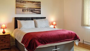 A bedroom with a bed, two bedside lamps, a nightstand, a wooden headboard, a painting, and a window with curtains.