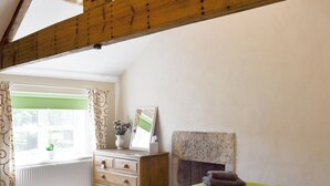 Une chambre à coucher comprenant un lit, une commode, un miroir, une cheminée et une fenêtre avec des rideaux.