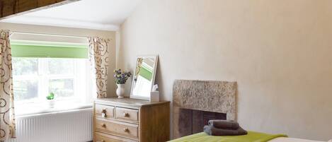 Un dormitorio con cama, cómoda, espejo, chimenea y ventana con cortinas.