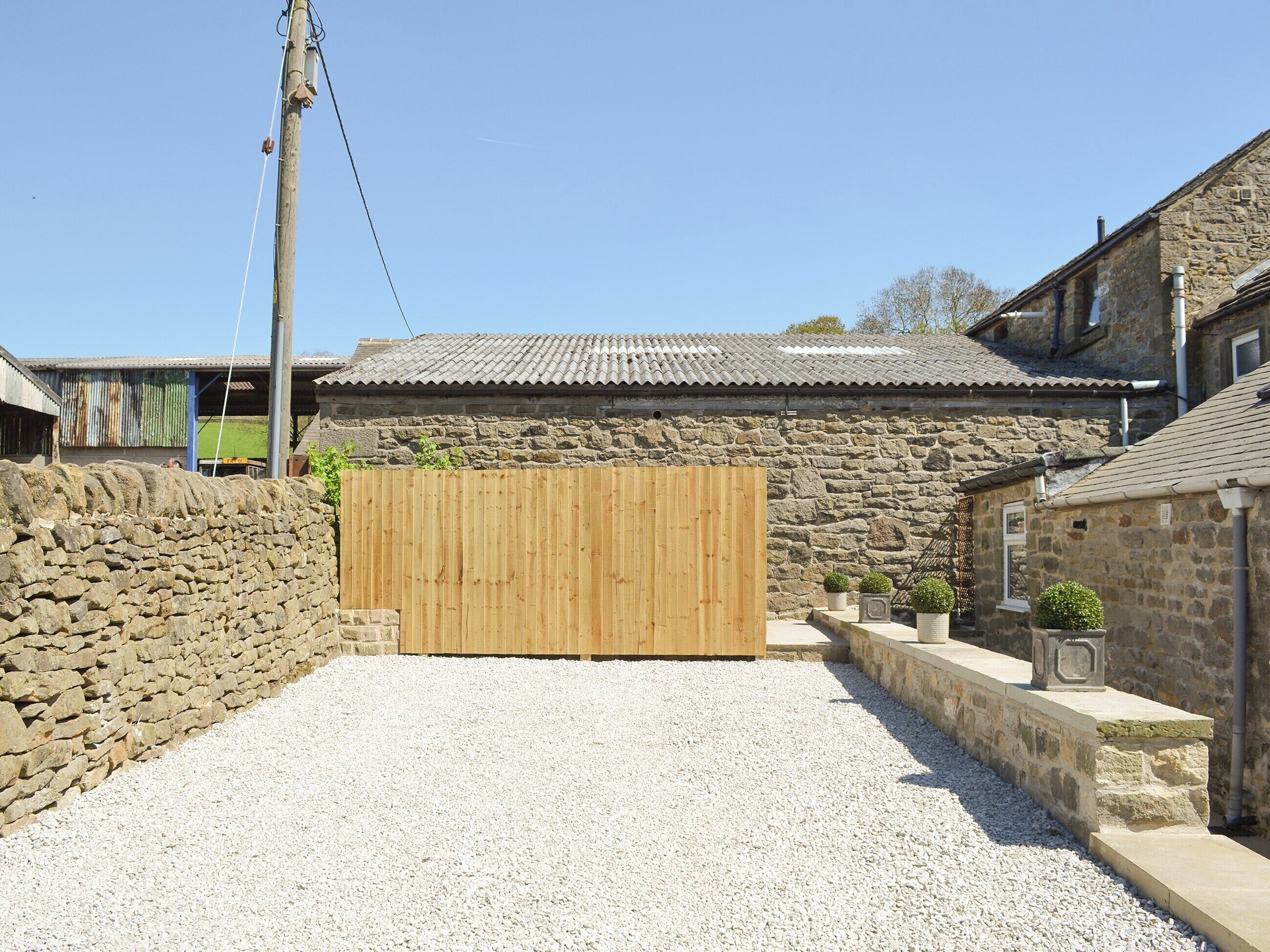 A stone building with a tiled roof, a wooden gate, and gravel ground.
