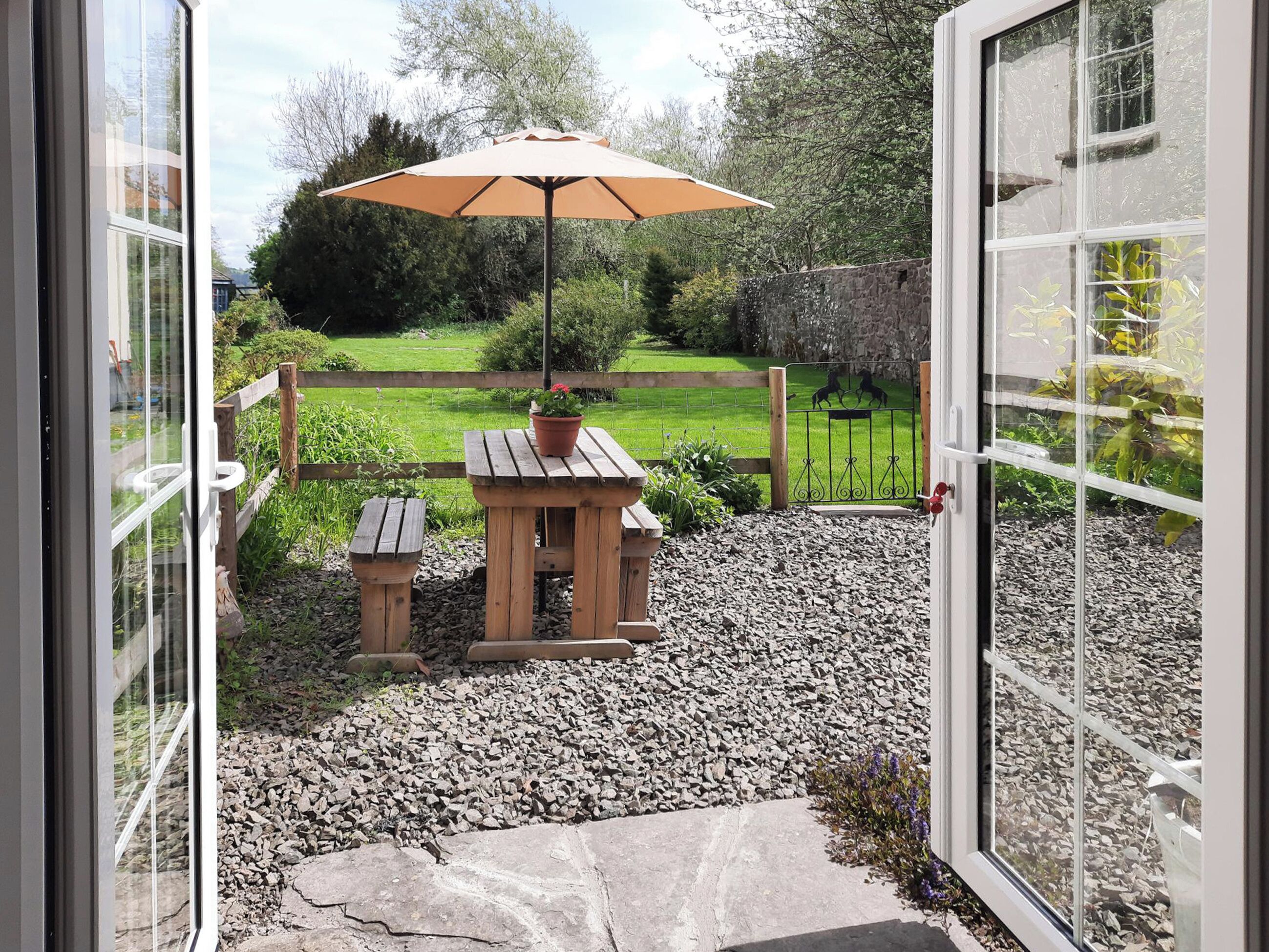 An open door leading to a patio with a wooden table, a bench, and a large umbrella.