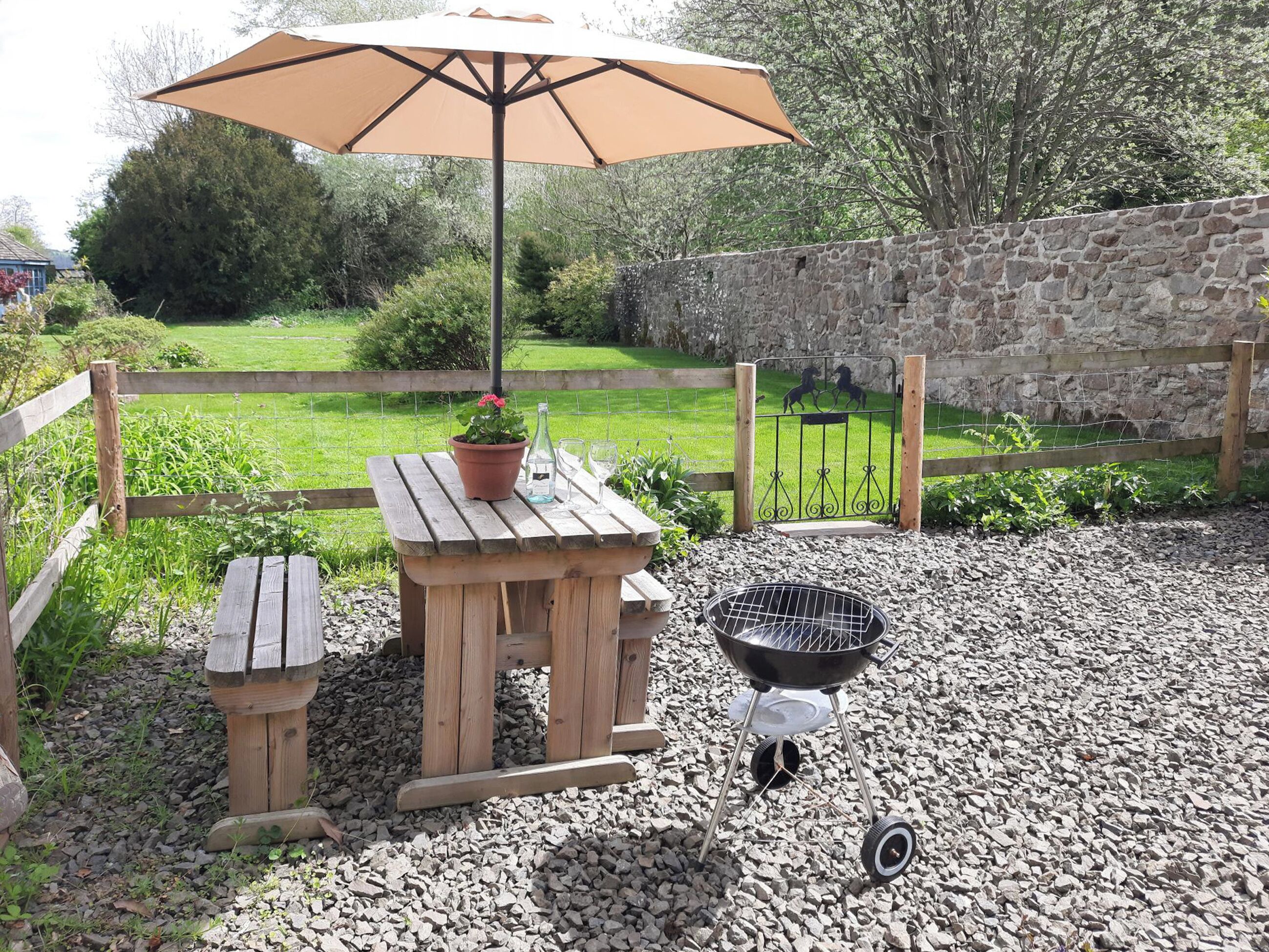 A wooden outdoor patio with a table, a bench, a barbecue grill, and a potted plant.