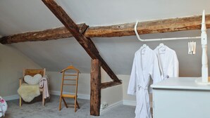 A room with a sloped ceiling, wooden beams, a white dresser, a chair with a fluffy white cushion, and a ladder. - 1 bedroom accommodation in Combe, near Presteigne (Combe, near Presteigne)
