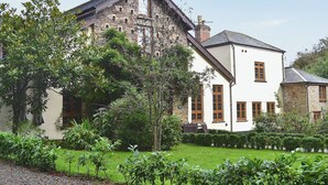 A two-story stone building with a white facade, a pitched roof, and a well-maintained garden with various plants and a gravel path. - 4 bedroom accommodation in Webbery, near Bideford (Webbery, near Bideford)