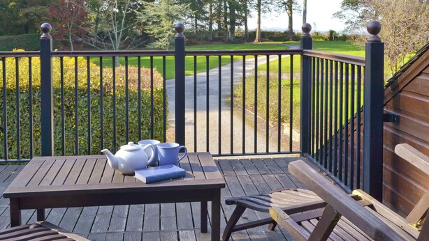 A wooden deck with a table and chairs, a metal railing, and a view of a green landscape. - 4 bedroom accommodation in Webbery, near Bideford (Webbery, near Bideford)