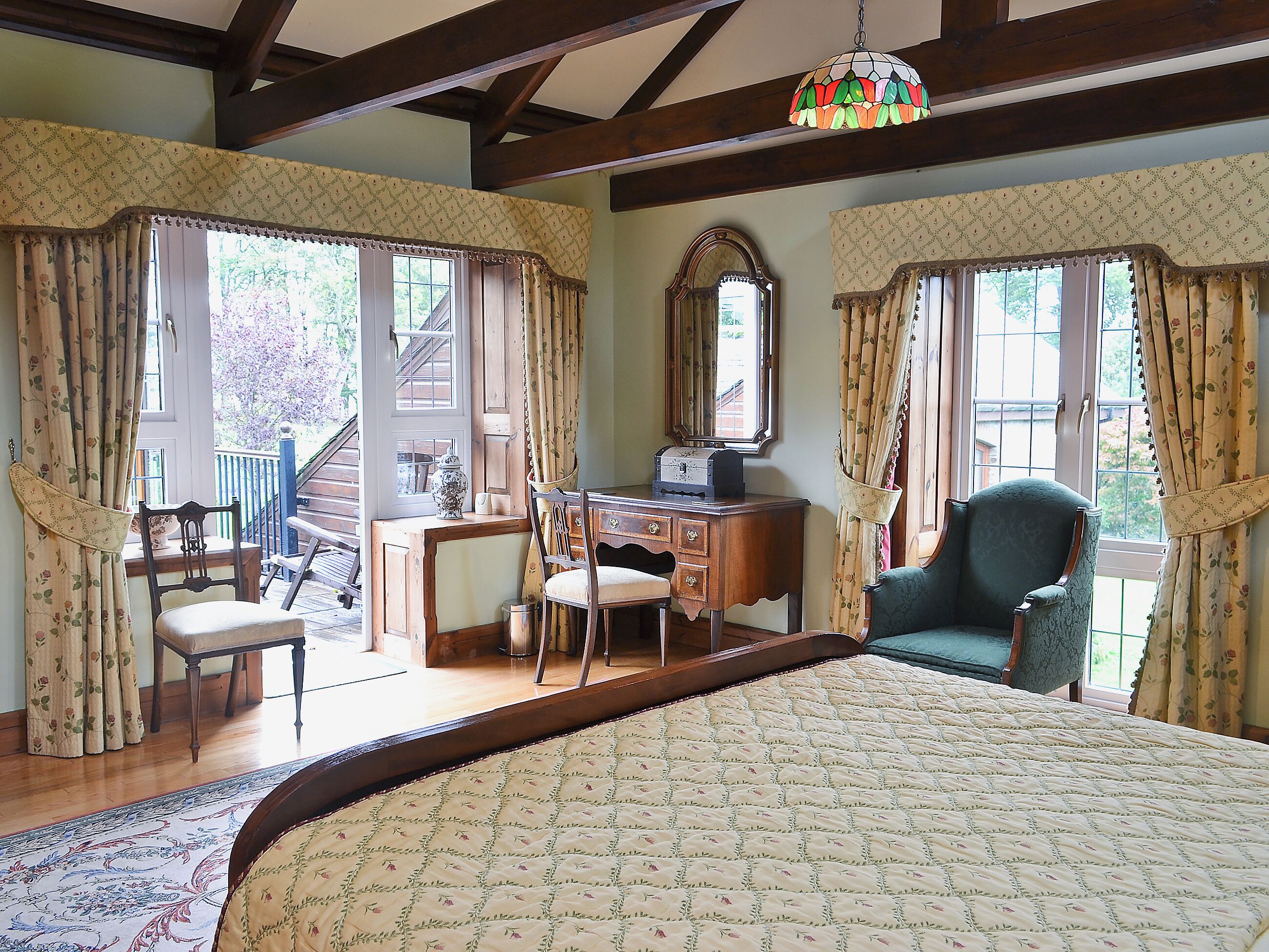 A bedroom with a bed, a desk, two chairs, a dresser, and a large mirror.