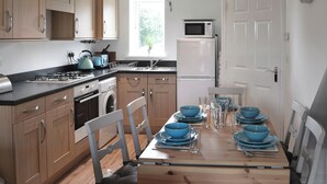 Una cocina moderna con gabinetes de madera, horno empotrado, microondas y lavamanos. Hay una mesa de comedor con cuencos y vasos azules.