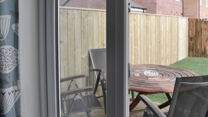 Un patio con una mesa redonda y sillas, una cerca de madera y una casa de ladrillo al fondo.