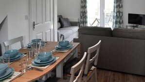 Un comedor con una mesa de madera dispuesta para cuatro personas, un sofá gris y un televisor al fondo.