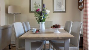A dining area with a table, chairs, a vase of flowers, a cake, and framed botanical prints on the wall.