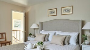 A neatly arranged bedroom with a bed, bedside tables, lamps, and framed pictures on the wall.
