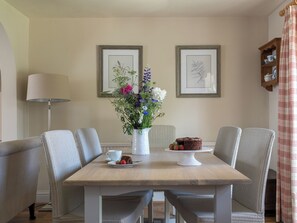 Uma área de refeições com mesa, cadeiras, um vaso de flores, um bolo e impressões botânicas emolduradas na parede.