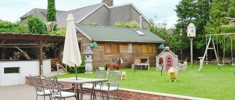 Eine Terrasse mit Tisch und Stühlen, ein Holzhaus mit grüner Dachbegrünung und eine Schaukel im Hintergrund.