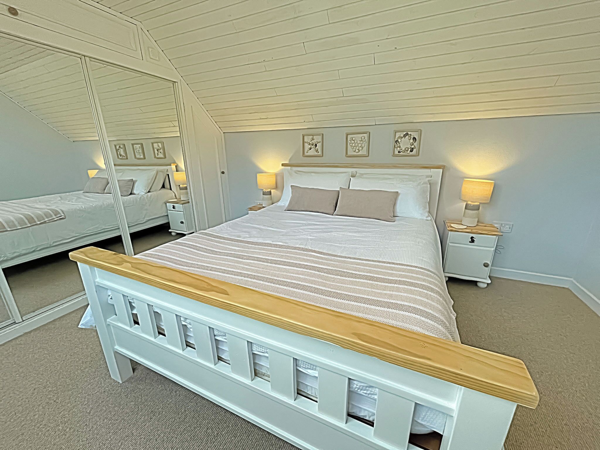 A bedroom with a large bed, two bedside tables with lamps, a mirror, and framed pictures on the wall.