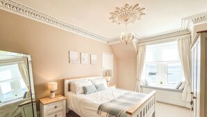 A bedroom with a bed, bedside tables, a mirror, and a window with curtains. - 4 bedroom accommodation in Millport, Isle of Cumbrae (Millport, Isle of Cumbrae)