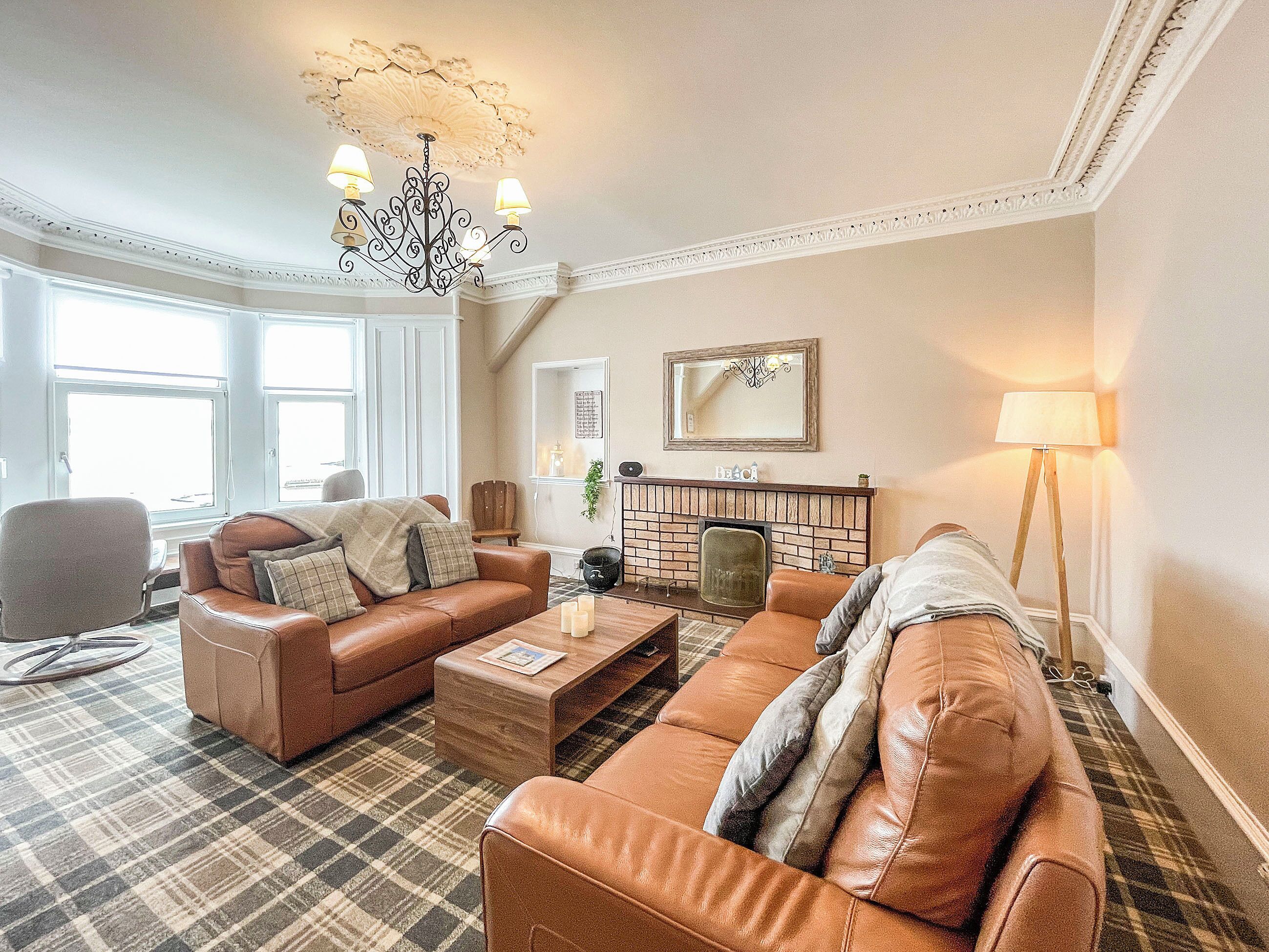 A living room with two leather sofas, a coffee table, a fireplace, and a chandelier. - 4 bedroom accommodation in Millport, Isle of Cumbrae (Millport, Isle of Cumbrae)