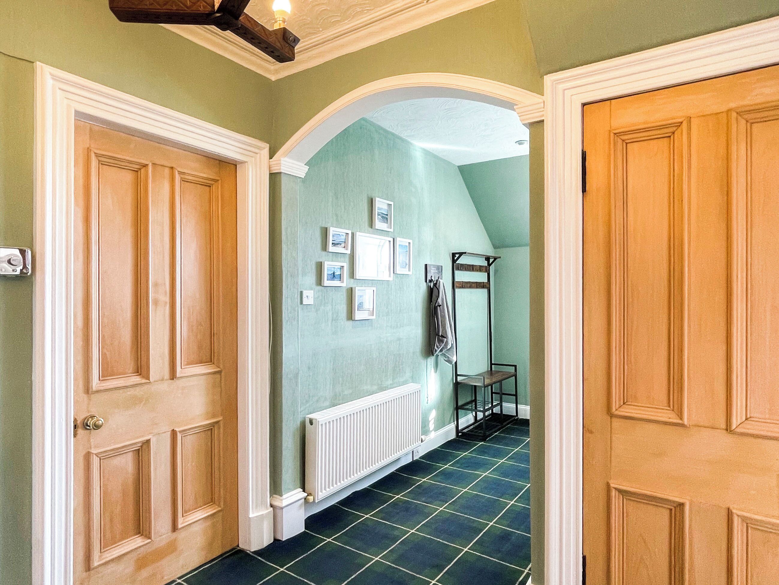 A hallway with a green wall, a radiator, and a rack with clothes.