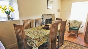 A dining room with a floral tablecloth, wooden chairs, a fireplace, and a patterned rug. - 4 bedroom accommodation in Cilan, near Abersoch (Cilan, near Abersoch)