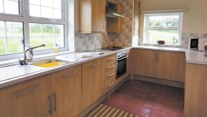 A kitchen with wooden cabinets, a stainless steel sink, and a tiled backsplash. - 4 bedroom accommodation in Cilan, near Abersoch (Cilan, near Abersoch)