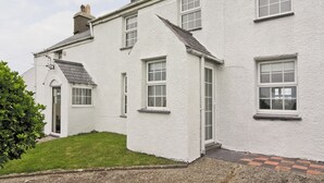 A white building with multiple windows, a door, and a small garden area. - 4 bedroom accommodation in Cilan, near Abersoch (Cilan, near Abersoch)