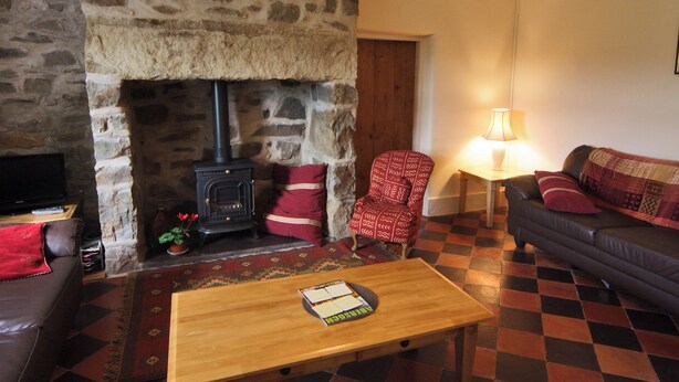 A cozy living room with a stone fireplace, a comfortable sofa, a wooden coffee table, and a television. - 4 bedroom accommodation in Cilan, near Abersoch (Cilan, near Abersoch)