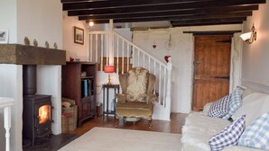 Ein gemütliches Wohnzimmer mit Kamin, einem weichen Sessel, einem weißen Sofa mit karierten Kissen und einer Holztreppe.