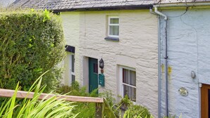Ein traditionelles Cottage mit einem geneigten Dach, einem kleinen Fenster und einer Tür mit grünem Rahmen.