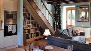 Un saló agradable amb una escala, una zona de dinar amb una taula preparada per a dues persones, i una biblioteca plena de llibres.