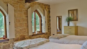 A bedroom with two beds, stone walls, and large arched windows.