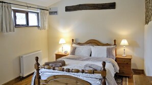 Ein hölzernes Himmelbett mit zwei Nachttischen, jeder mit einer Lampe. An der Wand ist eine Heizung angebracht, und ein Fenster mit Vorhängen ist sichtbar.