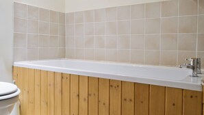 Un bagno con un mobile vanitario in legno, una vasca da bagno bianca e pareti rivestite di piastrelle color beige.