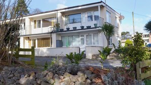 A two-story residential building with balconies, a stone wall in front, and a clear sky. - 2 bedroom accommodation in Dawlish Warren (Dawlish Warren)