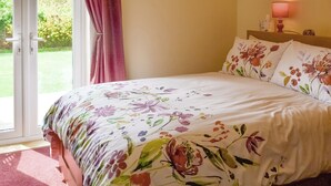 Une chambre à coucher avec un lit, une couvre-lit à motifs floraux, une fenêtre avec des rideaux et une lampe de chevet.