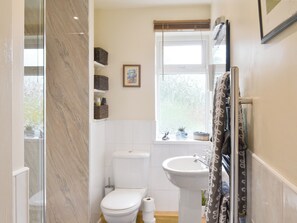 A bathroom with a toilet, sink, and window. There are wicker baskets on the wall and a framed picture above the toilet. - 1 bedroom accommodation in Alnwick (Alnwick)