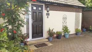 Une maison avec une porte d’entrée noire, un mur en briques et plusieurs plantes en pot.