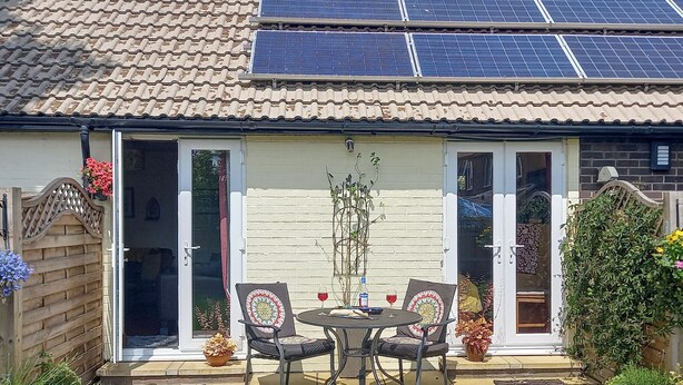 Une terrasse avec une table et des chaises, une plante en pot et un panneau solaire sur le toit.