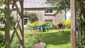 Une maison en pierre avec un jardin, un espace extérieur aménagé pour s’asseoir et un coin barbecue.