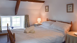Une chambre à coucher avec un lit, une table de chevet, une lampe et une fenêtre avec des rideaux.