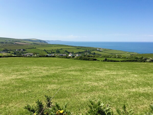 Un paysage rural caractérisé par des collines douces, une vue sur la côte et des maisons dispersées.