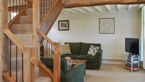 Un escalier avec des rampes en bois menant à un niveau supérieur, un canapé vert avec des coussins, une table basse et un téléviseur posé sur un meuble.