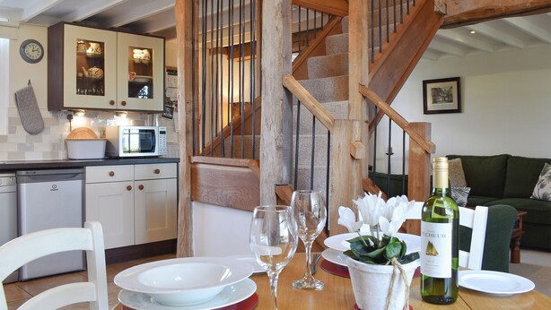 Un espace repas avec un escalier en bois, une cuisine équipée de meubles et un canapé vert en arrière-plan.