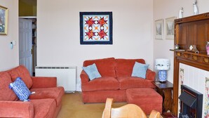 A living room with two red sofas, a ceiling fan, a fireplace, and a quilt on the wall. - 2 bedroom accommodation in Ambleside (Ambleside)