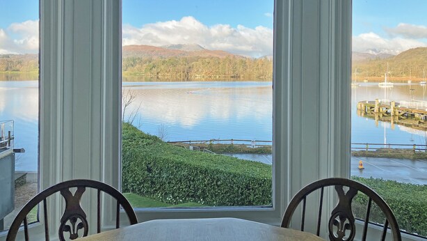 A view through a window of a lake with boats, a dock, and a mountainous landscape. - 2 bedroom accommodation in Ambleside (Ambleside)