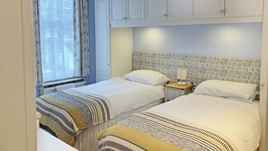 A bedroom with two beds, a window with curtains, a bedside table with a lamp, and a wardrobe. - 2 bedroom accommodation in Ambleside (Ambleside)