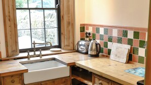 A kitchen with wooden cabinets, a sink, a window, and a tiled backsplash. - Langcliffe Lock Cottage (Langcliffe, near Settle)