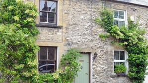 A stone building with two windows, a green door, and overgrown vegetation. - Langcliffe Lock Cottage (Langcliffe, near Settle)