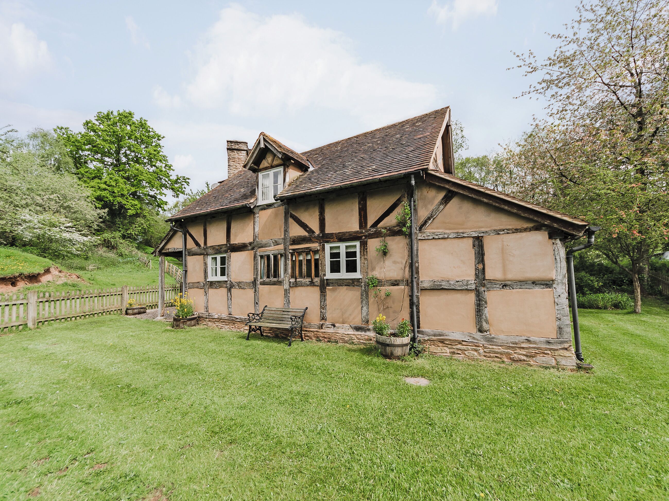A traditional half-timbered house with a sloped roof, a wooden bench, and a stone foundation.