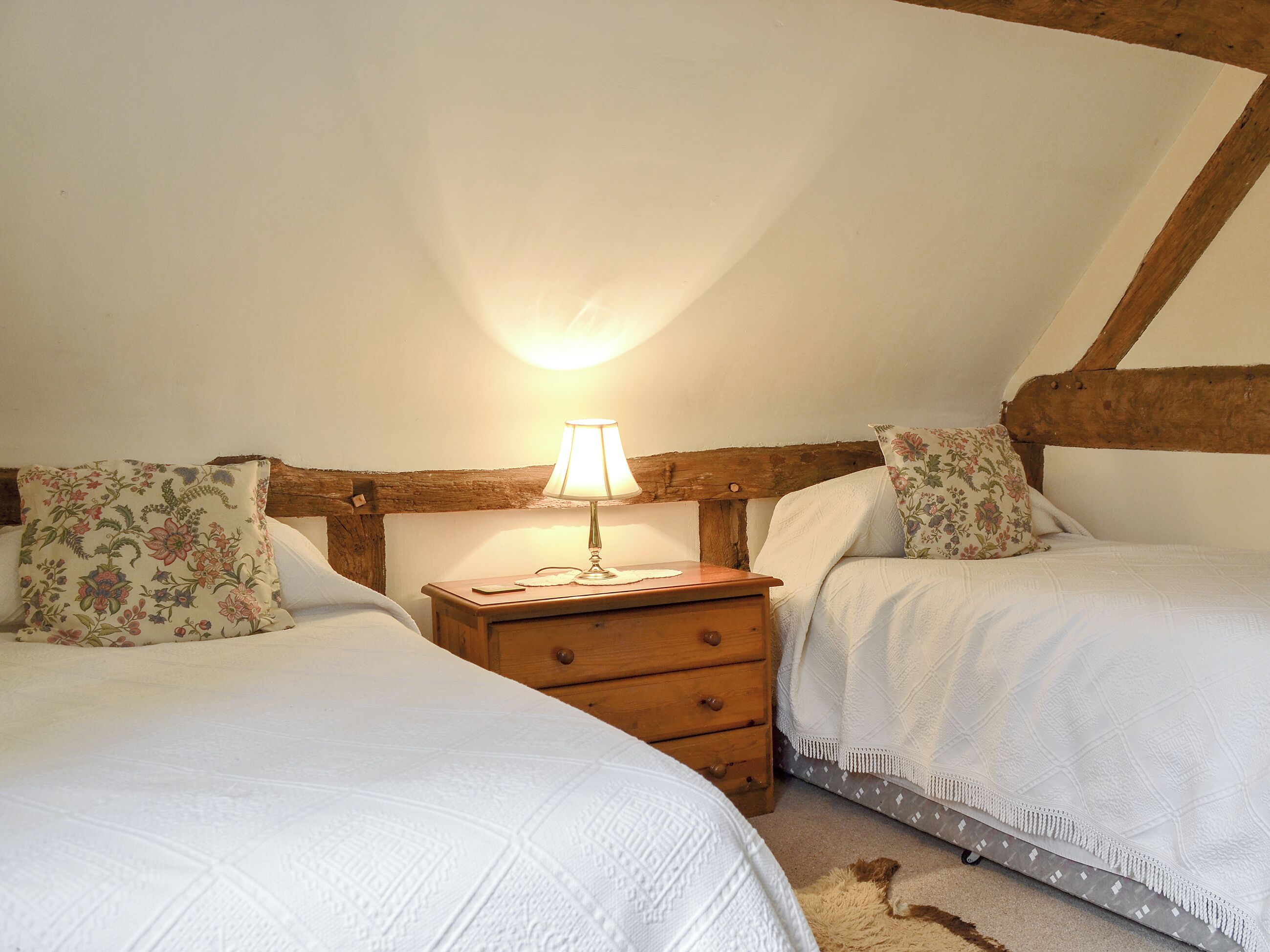 A bedroom with two beds, a nightstand with a lamp, and a wooden headboard.