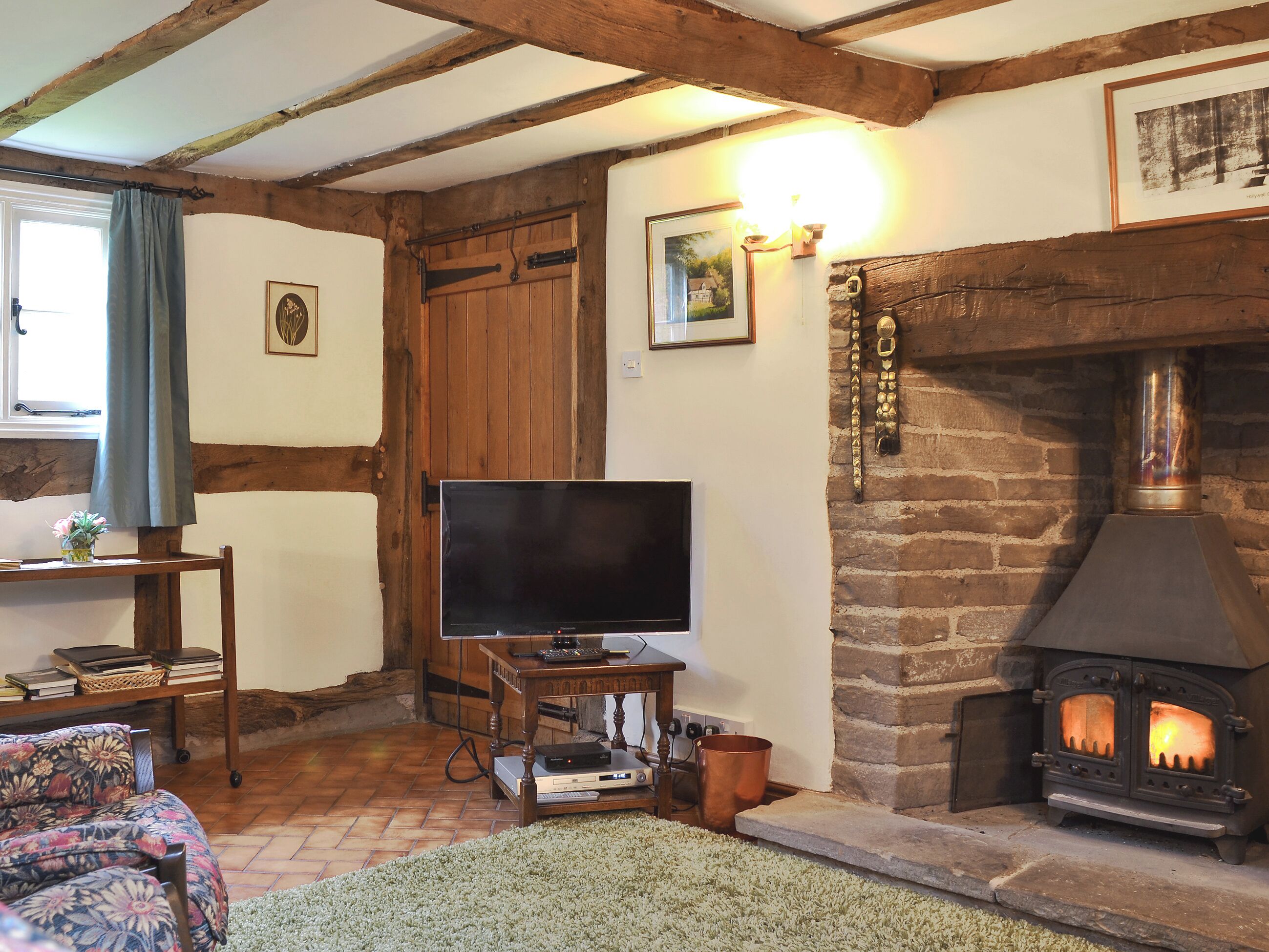 A cozy living room with exposed wooden beams, a fireplace, a television, and a rustic stone wall.