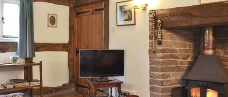 A cozy living room with exposed wooden beams, a fireplace, a television, and a rustic stone wall.